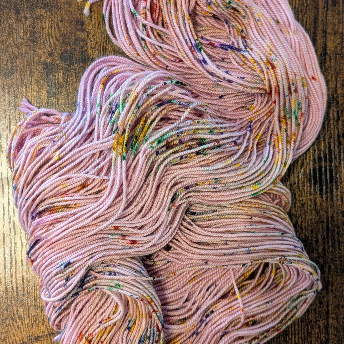 Pink yarn with multicolored speckles on a wooden surface