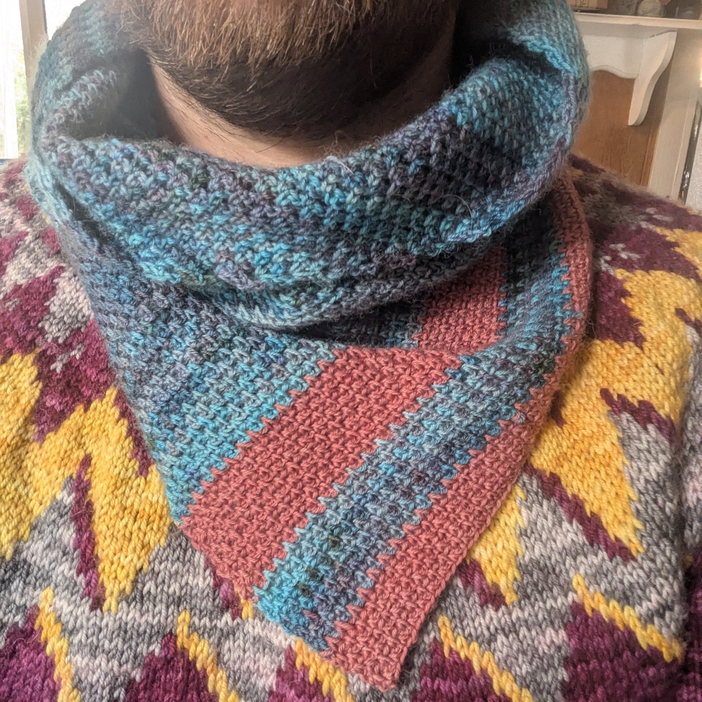 Person wearing a colorful patterned sweater with a patterned scarf.
