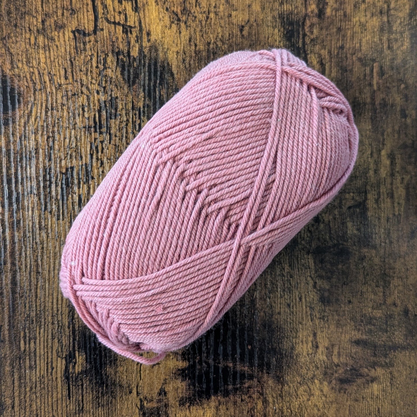 Pink skein of yarn on a textured wooden surface