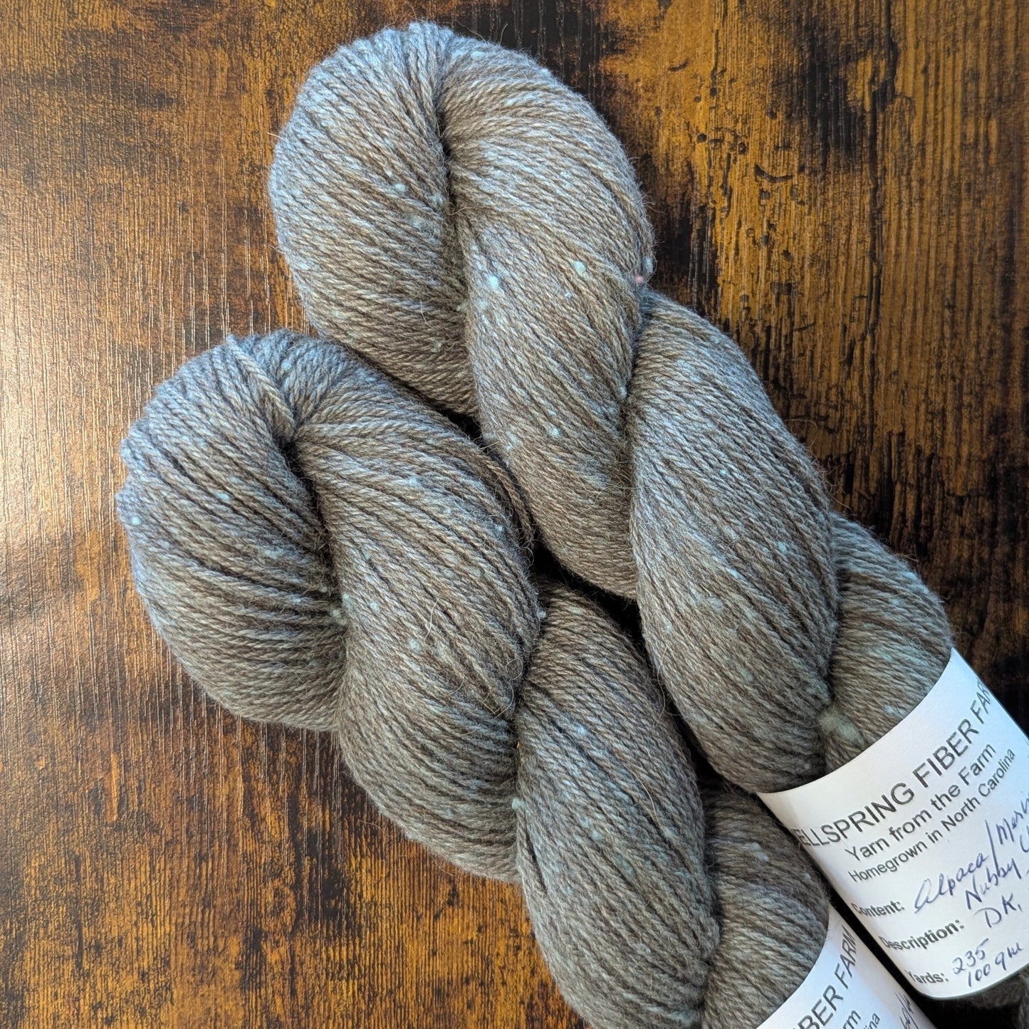 Two skeins of gray yarn with labels on a wooden surface