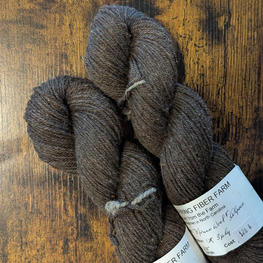 Two skeins of brown yarn with labels on a wooden surface