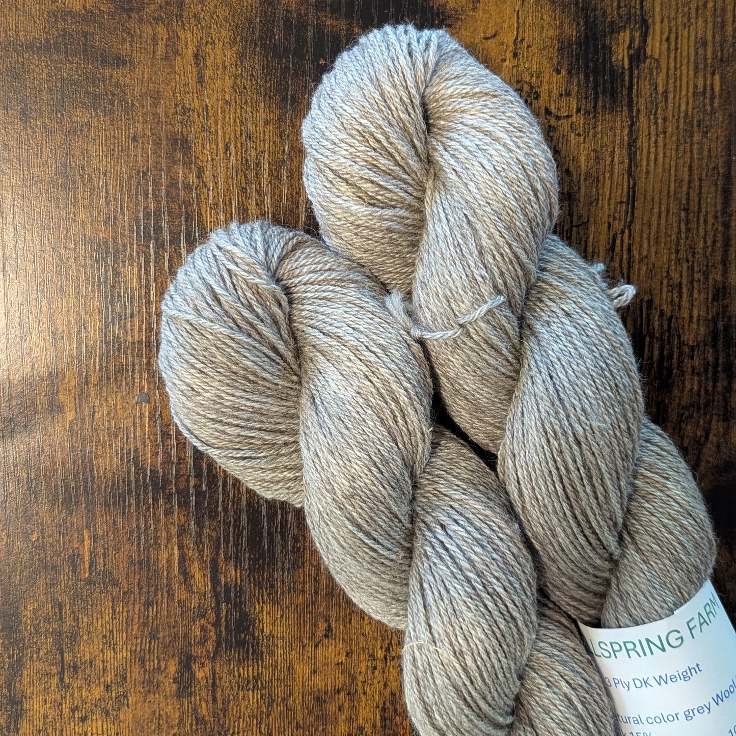 Three skeins of yarn on a wooden surface with a label.