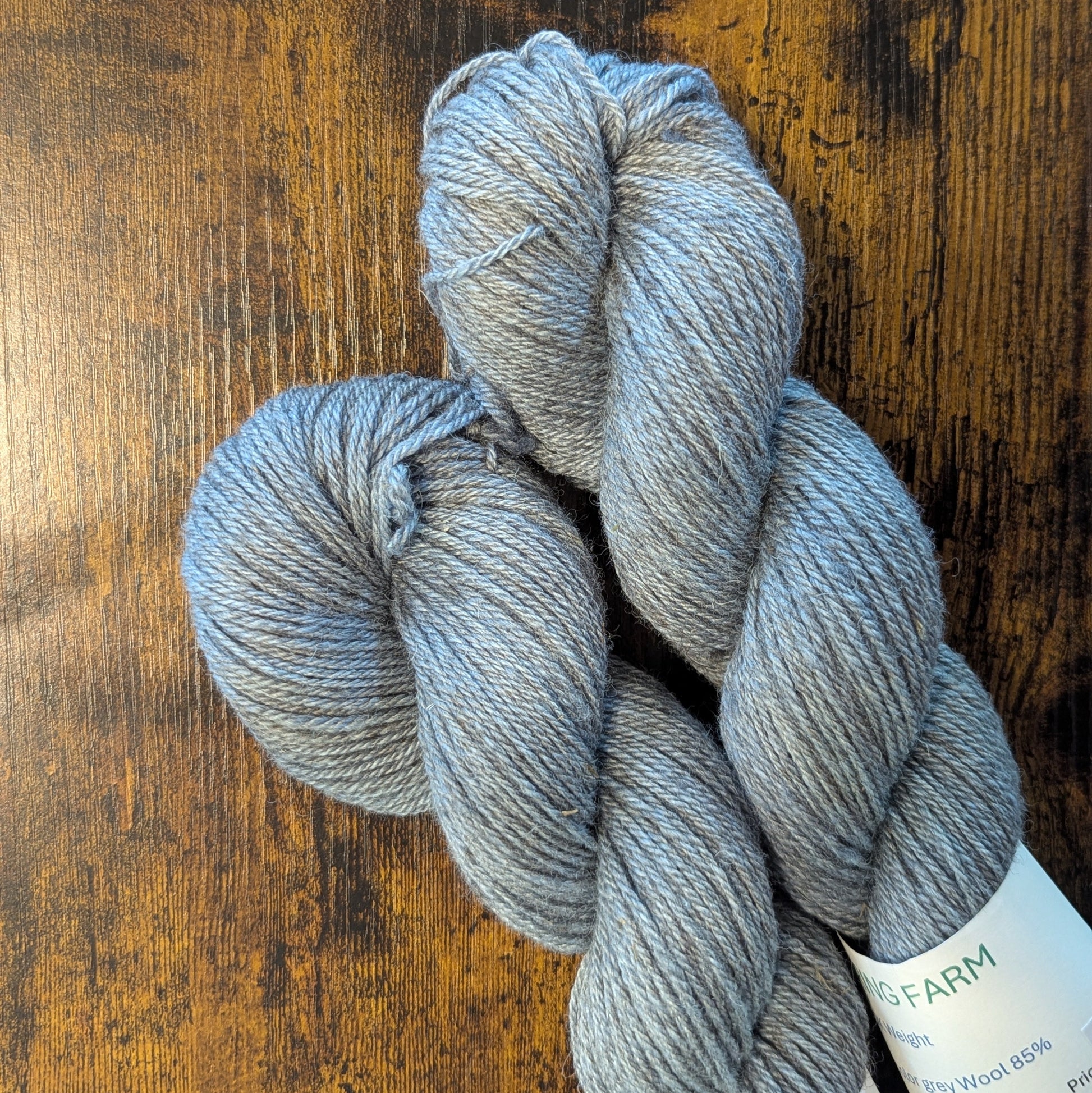 Three skeins of gray yarn on a wooden surface with a label visible.