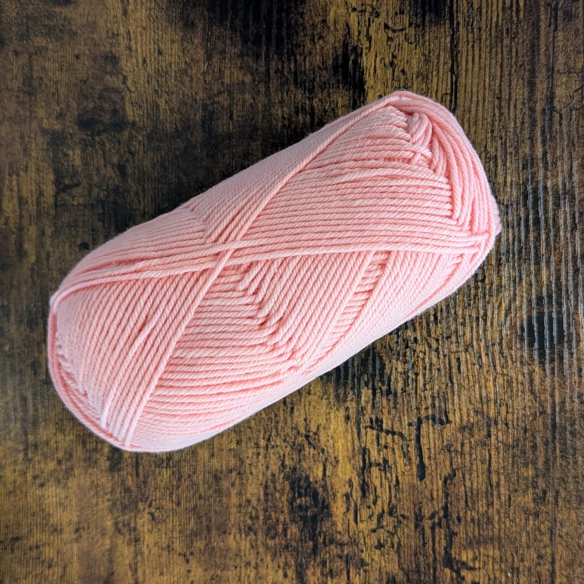 Pink yarn ball on a textured wooden surface